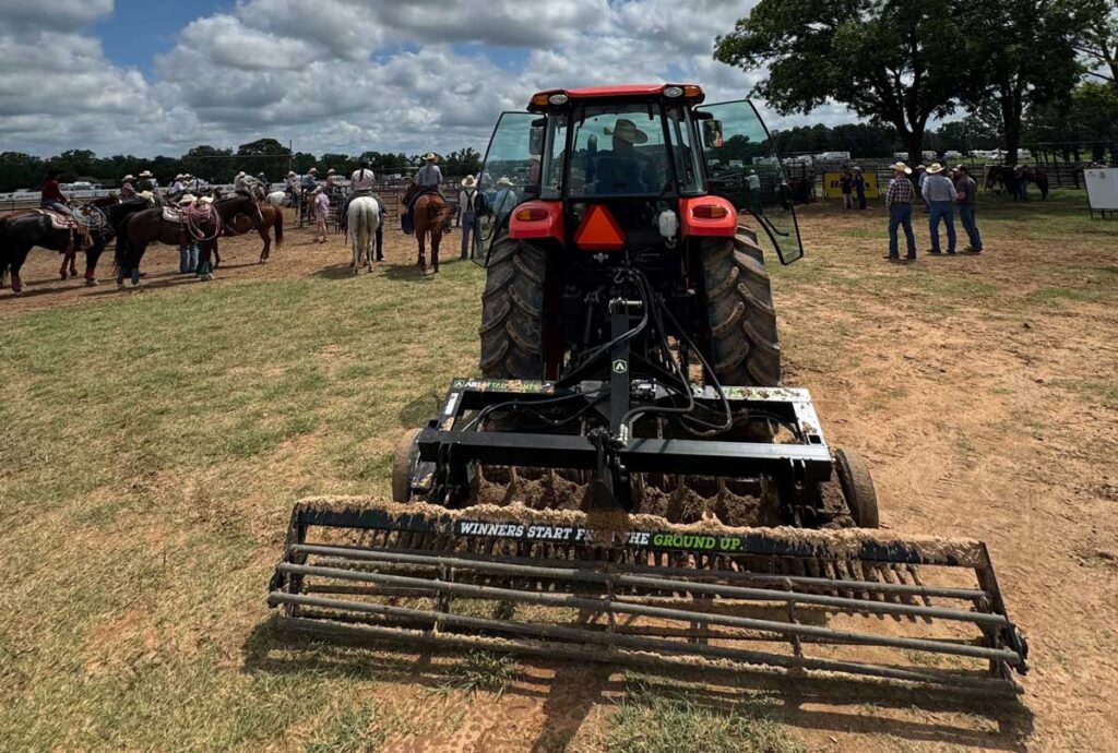 ABI Attachments TR3 Rodeo Arena Drag displayed in front of a rodeo crowd, showcasing rolling basket, adjustable scarifiers, auto-leveling blade.