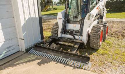 Skid steer loader attachment in use by a house.