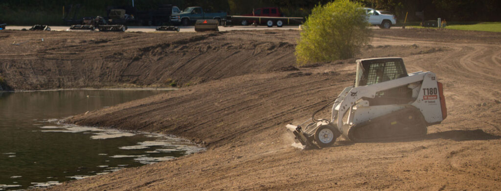 Skid steer attachment attached to a skid steer on dirt/soil.