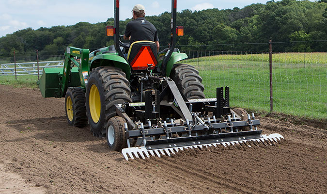 TR3 is being used in the soil/dirt while being attached to a large green tractor.