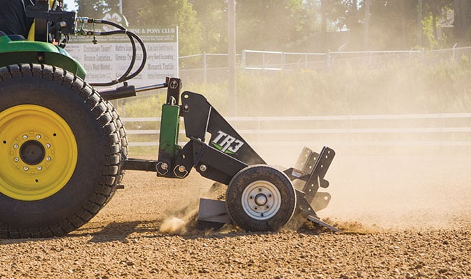 TR3 arena drag being pulled across the ground by a green tractor.