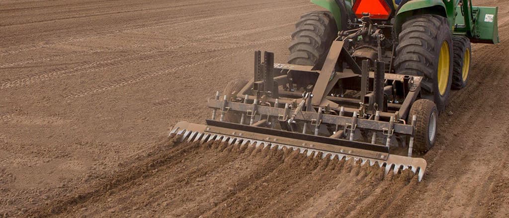 Natural footing arena drags being pulled from a green tractor.