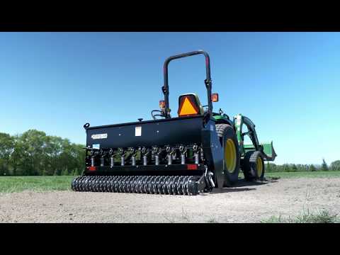 Tractor displaying seeder outdoors on gravel, near grass.
